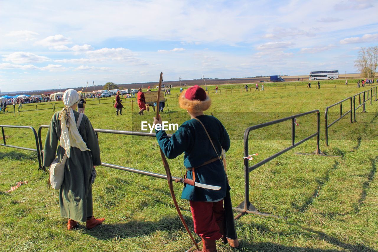 REAR VIEW OF MAN IN FIELD AGAINST SKY