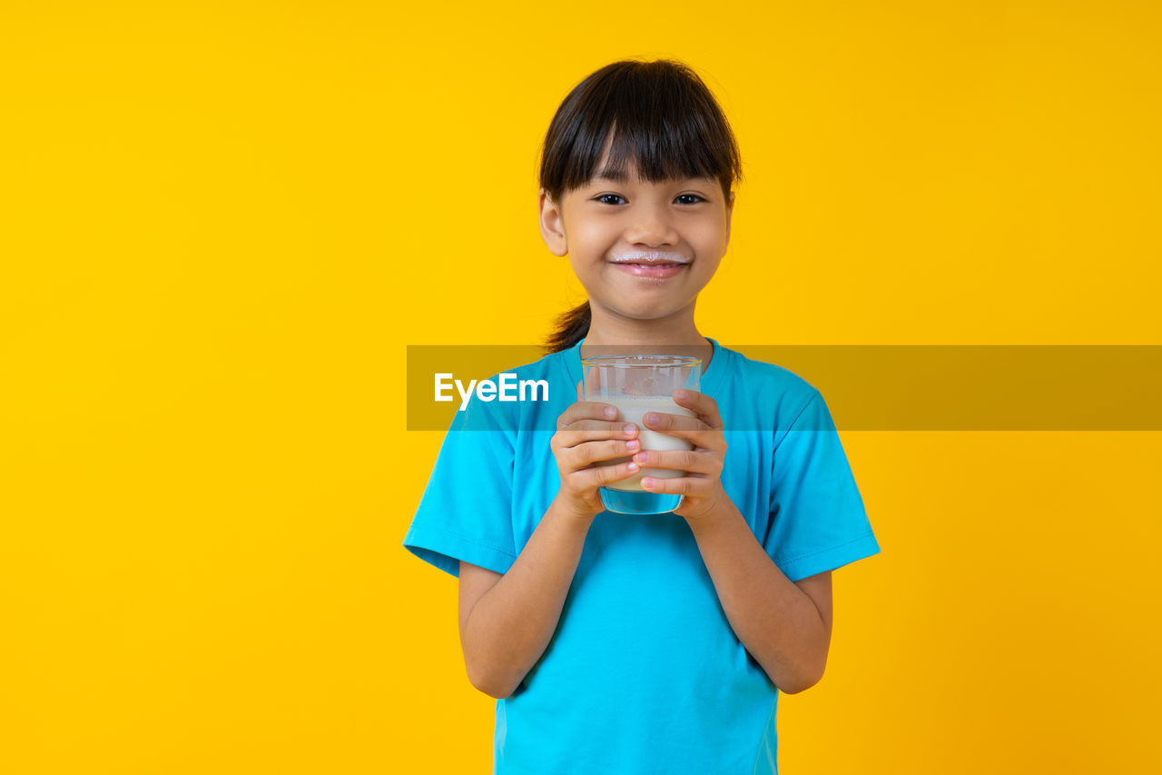 PORTRAIT OF SMILING BOY STANDING ON YELLOW GLASS