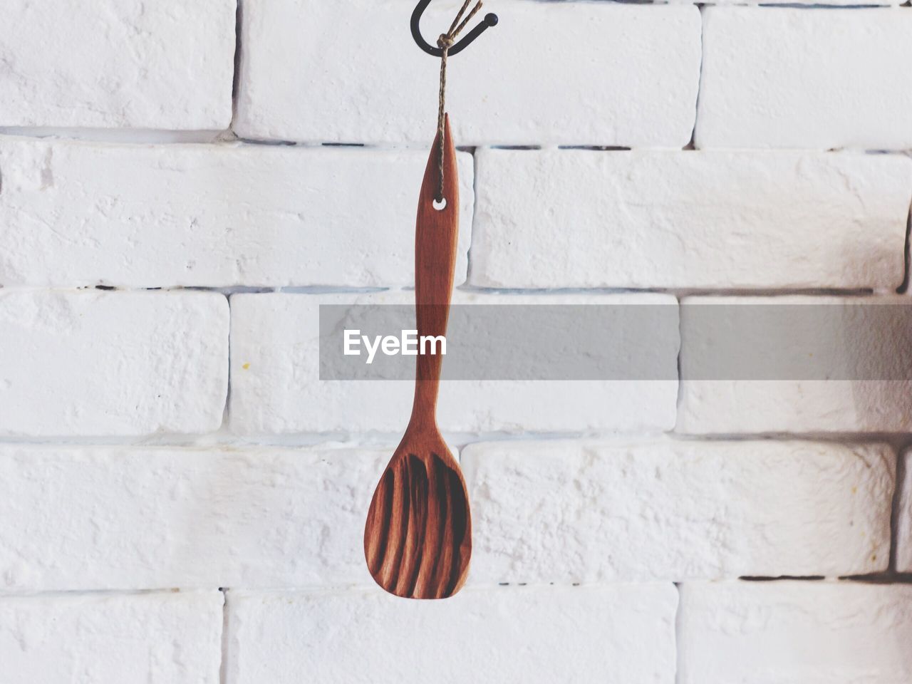 Close-up of wooden spoon hanging against white wall