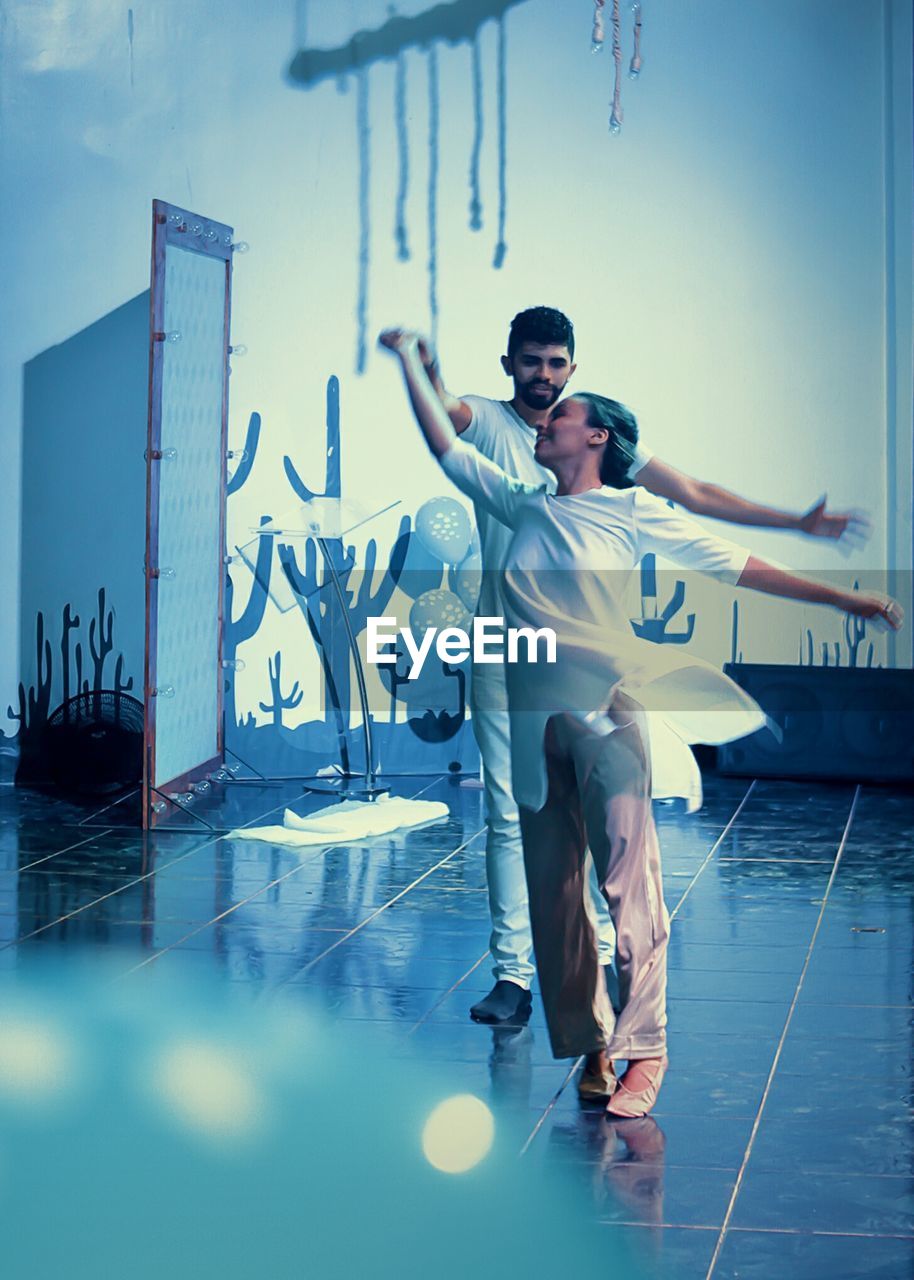 Full length of smiling dancers practicing on tiled floor against wall at studio