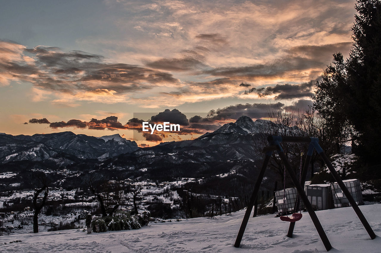 Swing on snow covered field by mountains against sky during sunset