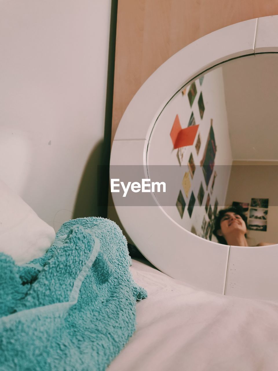 Woman looking on her reflection in the mirror on bed at home