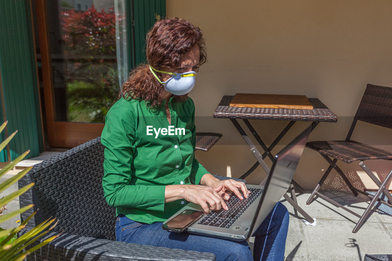 Woman with antivirus mask working with laptop in a garden. people life during the pandemic