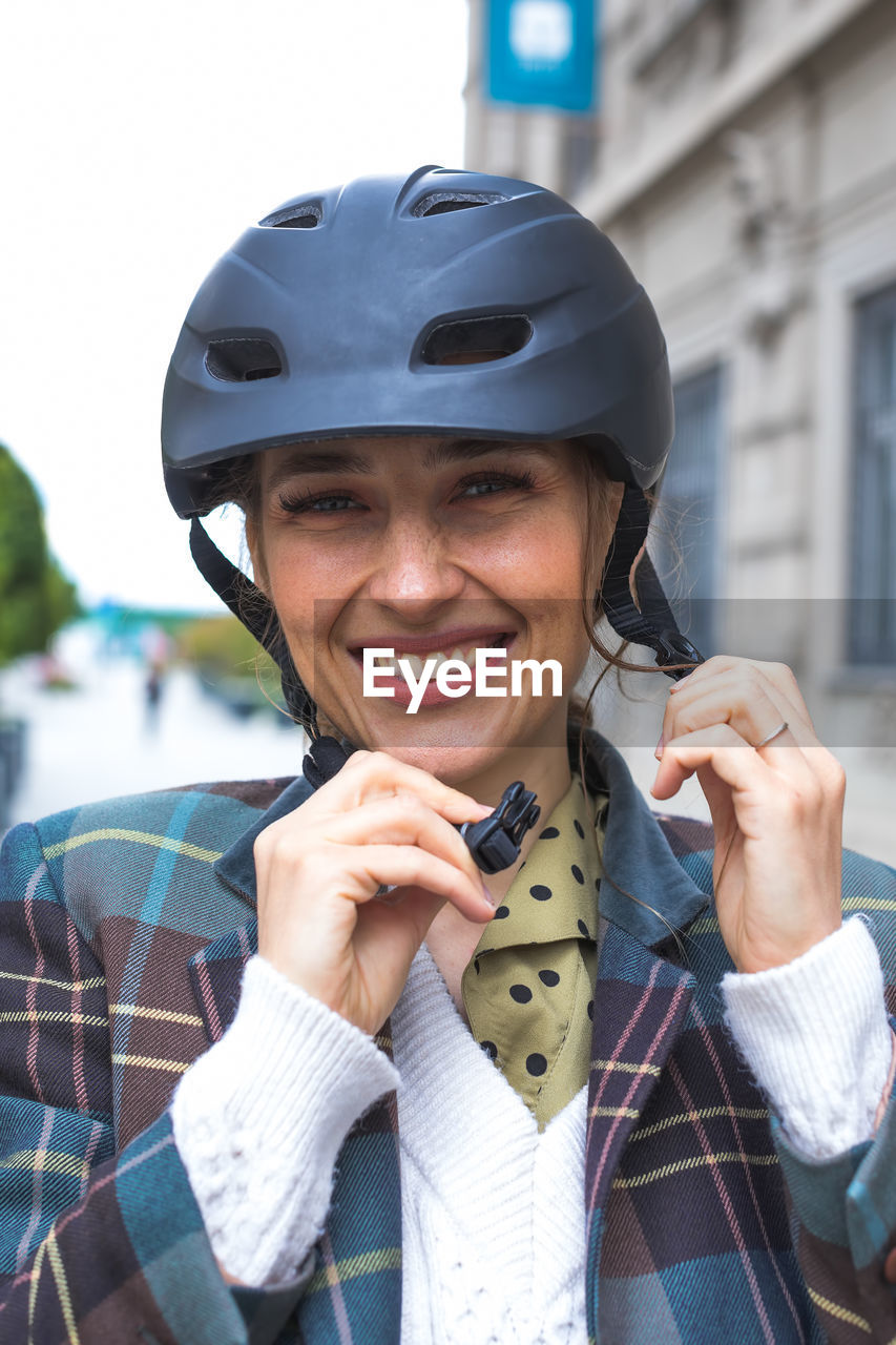 Portrait of young woman putting bicycle protective helmet