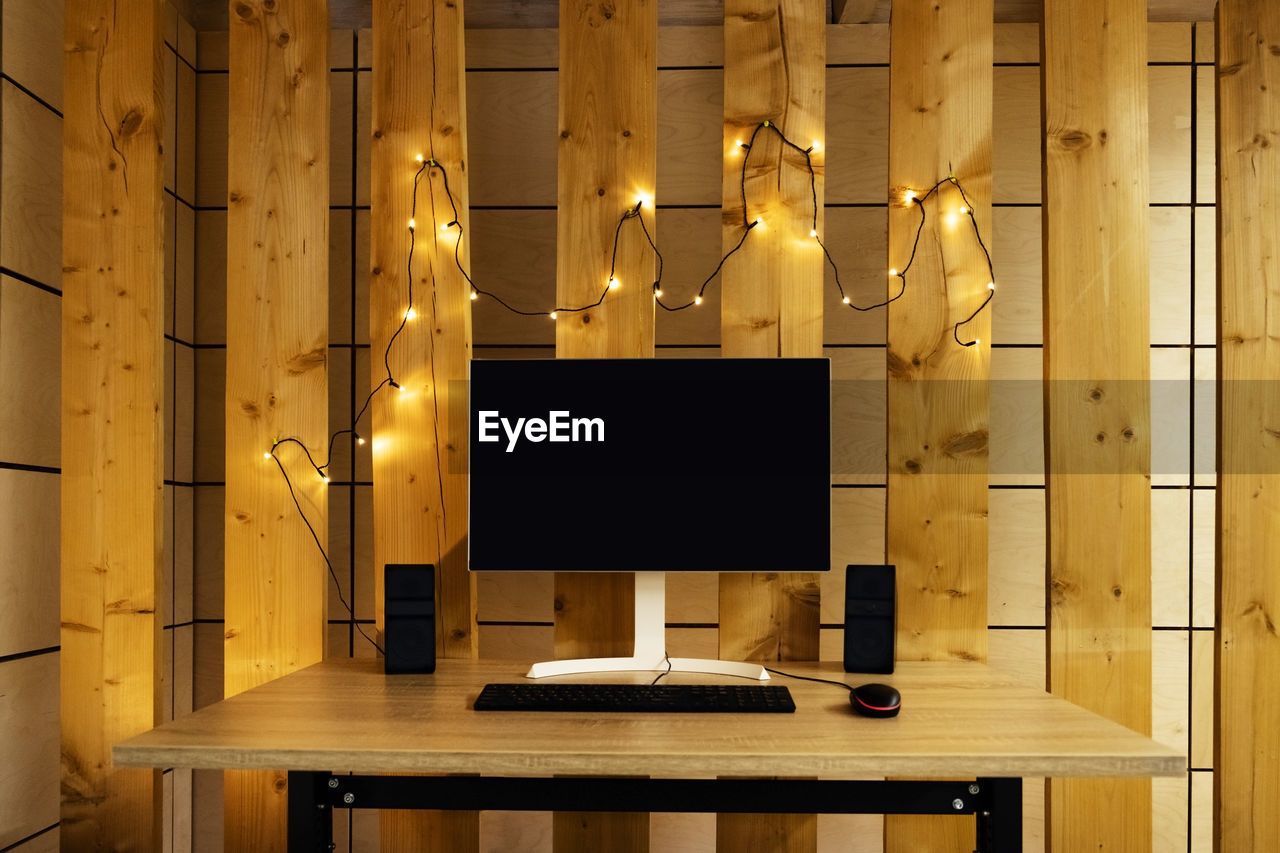 Home workplace - large monitor, speakers and lights on wooden walls. 
