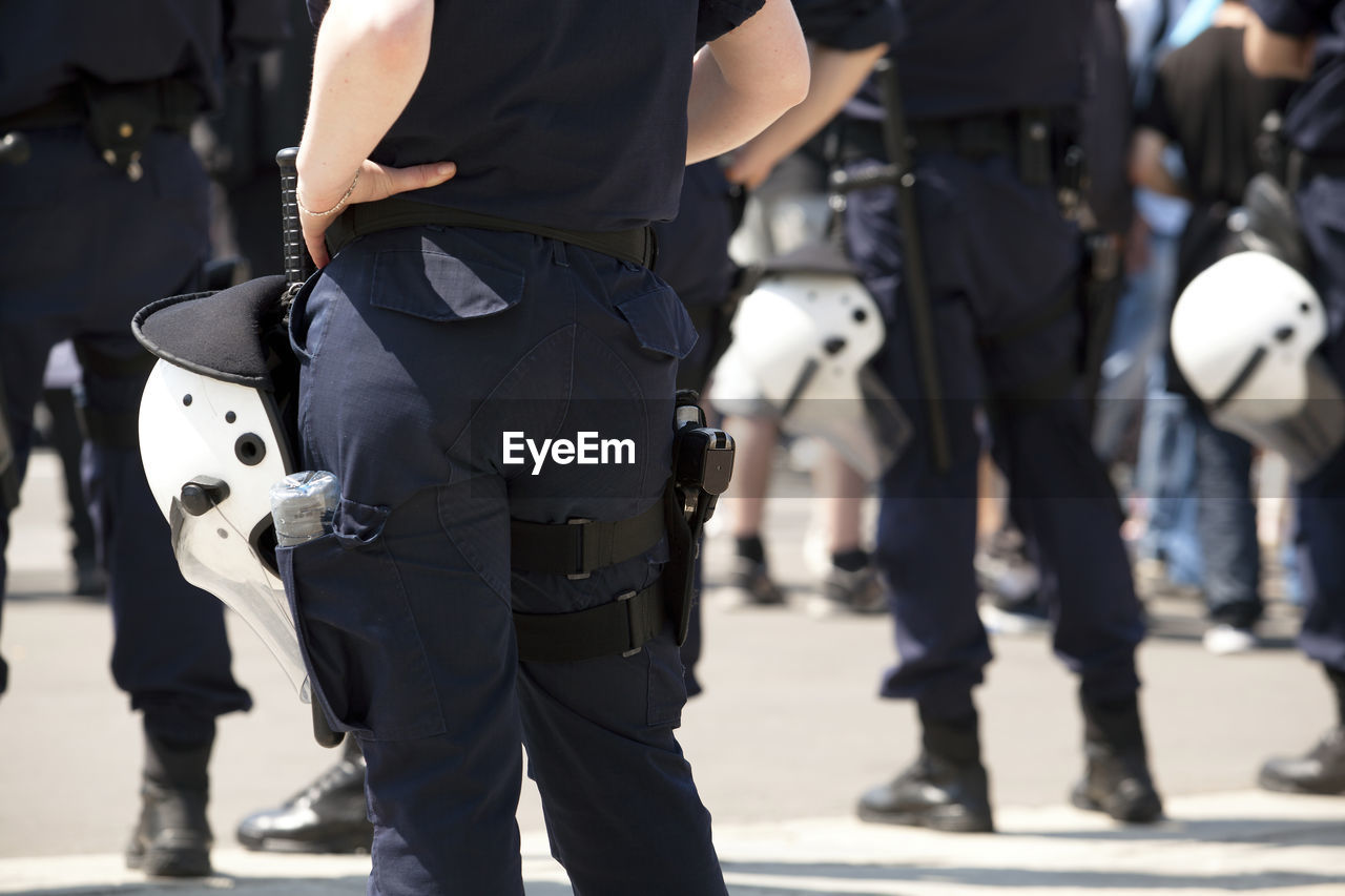 Rear view midsection of female police officer standing with hand on hip