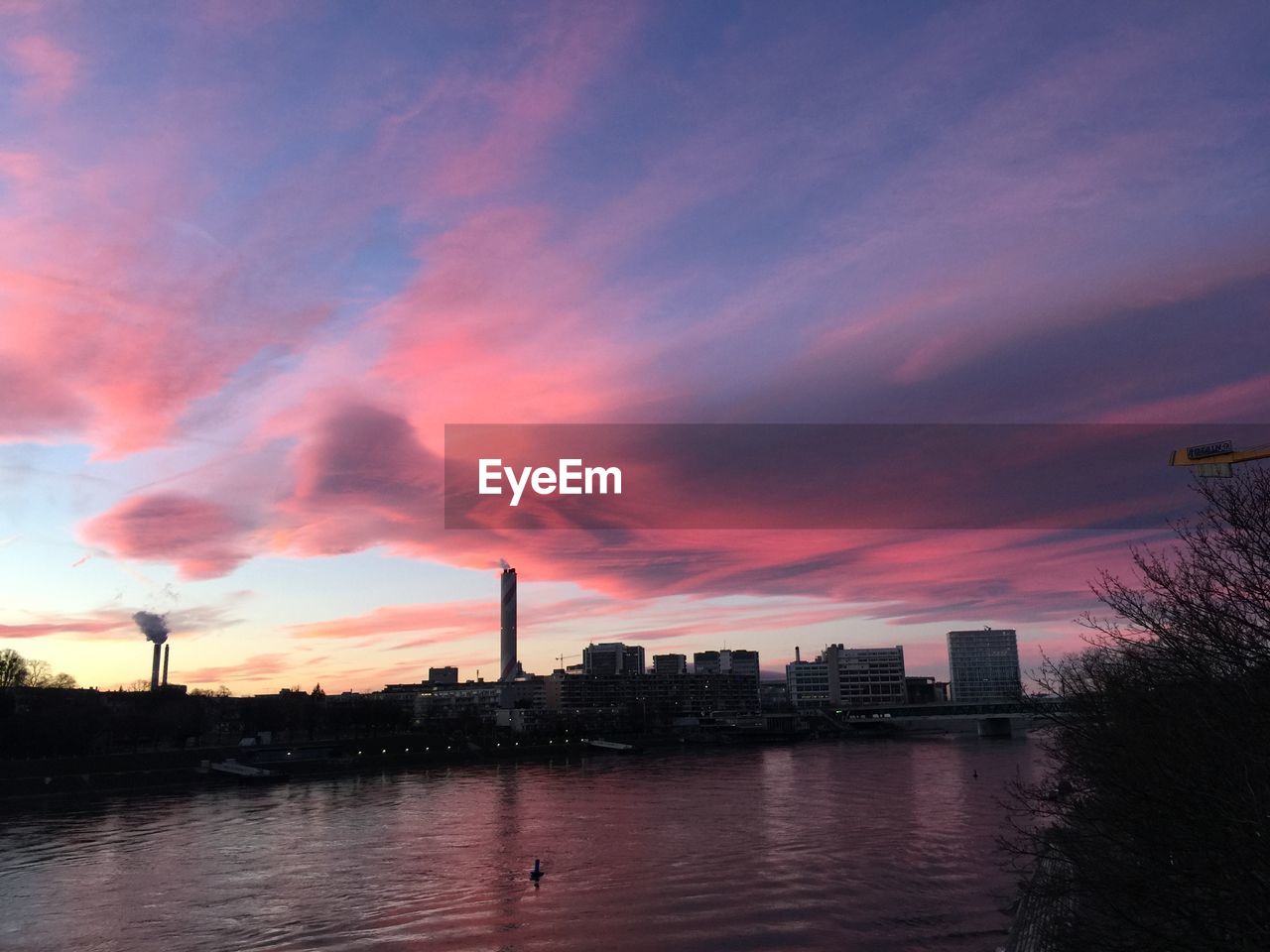 Silhouette buildings by river against sky during sunset in basel