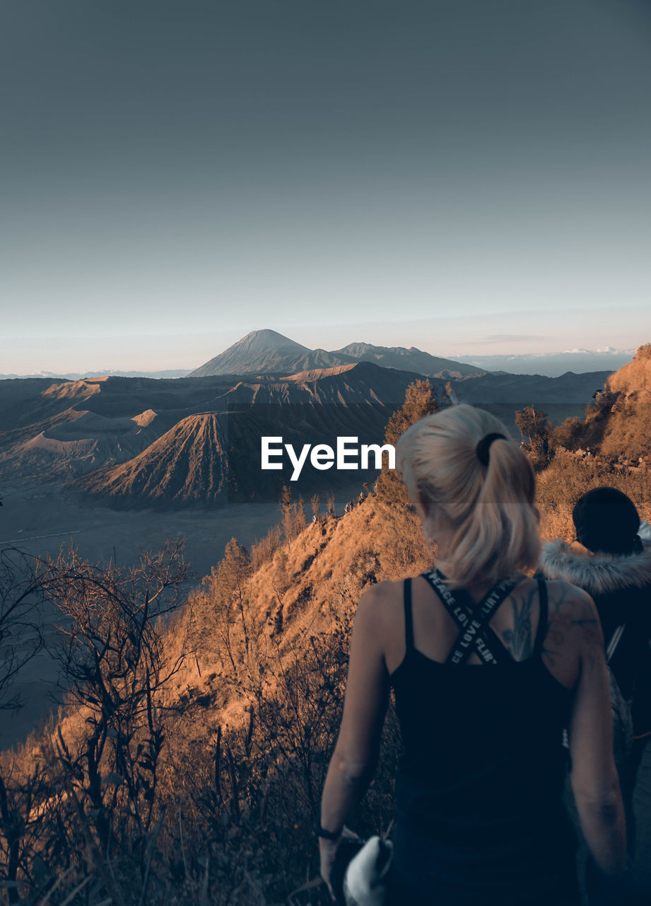 Rear view of woman standing on mountain against clear sky