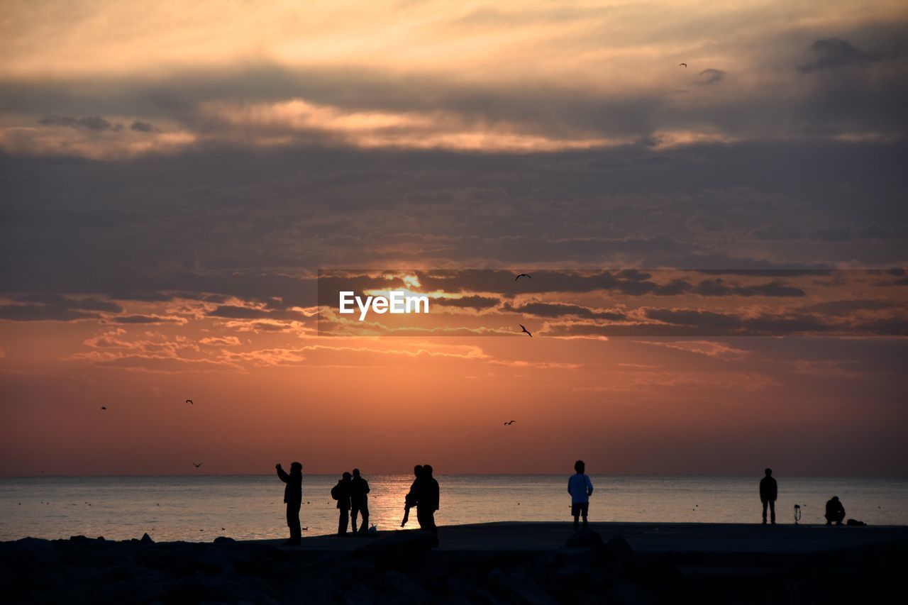 People standing on field against cloudy sky during sunset