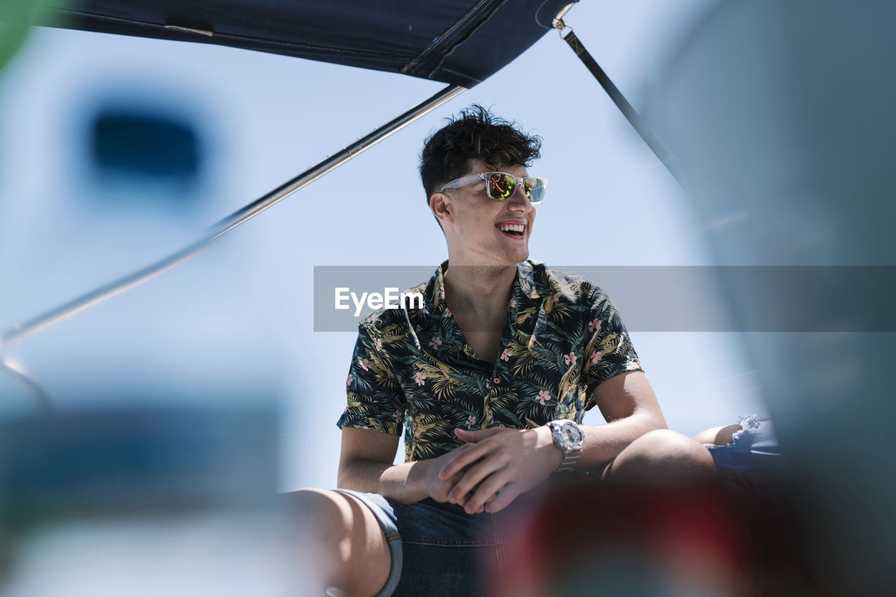 Young man laughing while sitting in yacht during sunny day