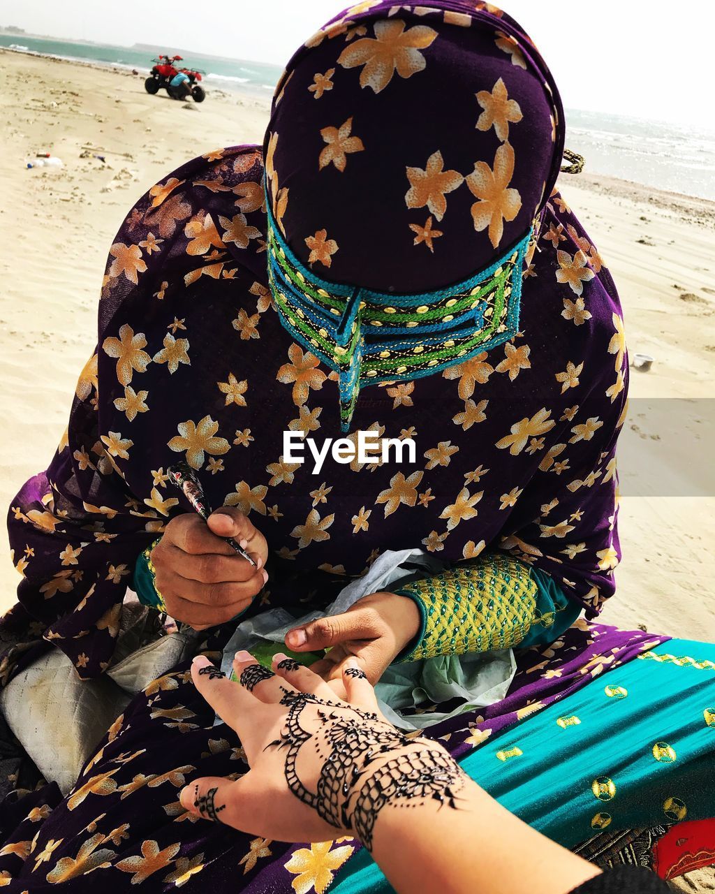 Woman applying henna tattoo on cropped hand at beach