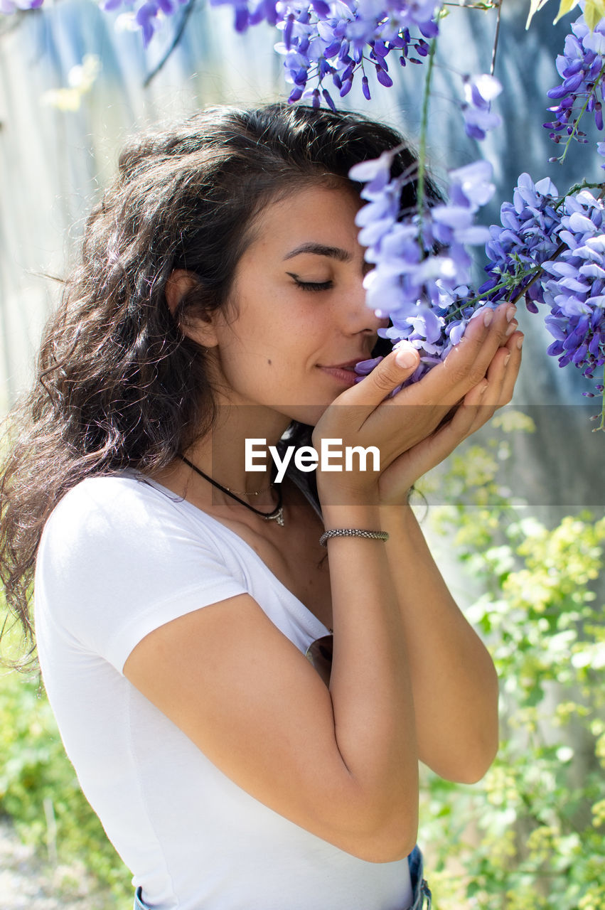 Side view of young woman smelling flowers on plants