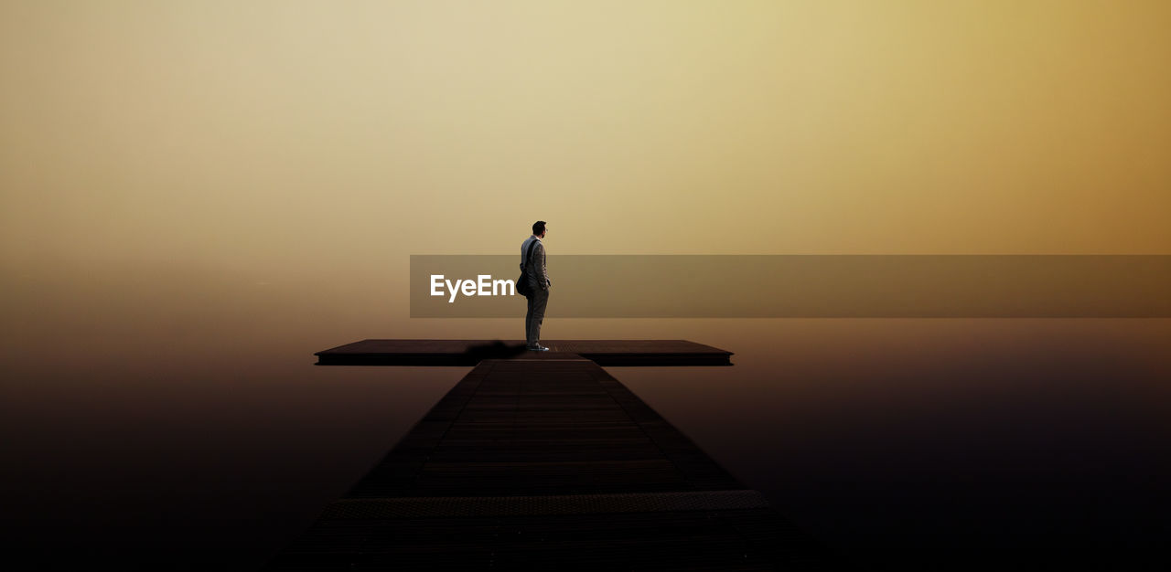 Man standing on pier over lake during sunset