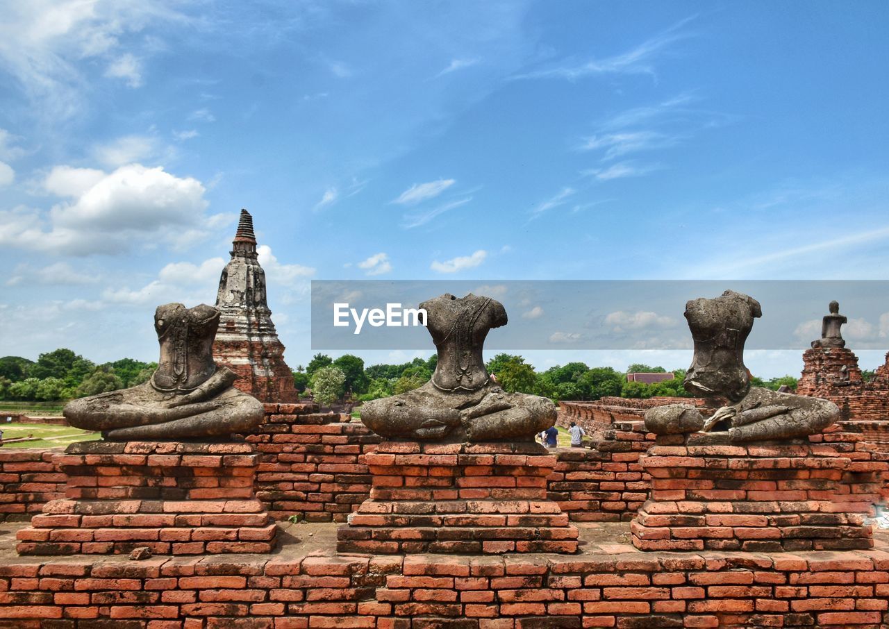 Broken buddha statues against cloudy sky