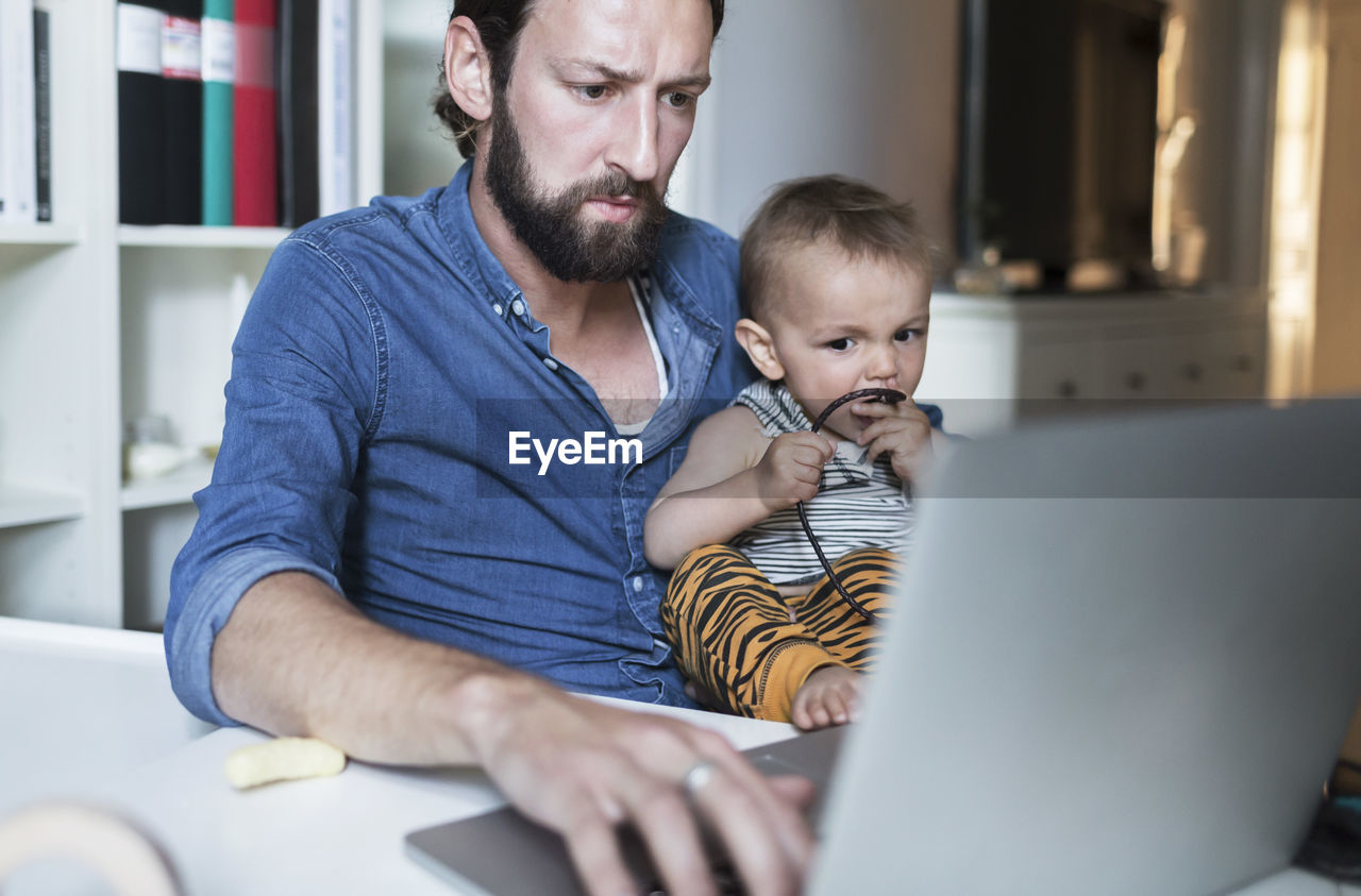 Mid adult businessman using laptop while taking care of baby at home