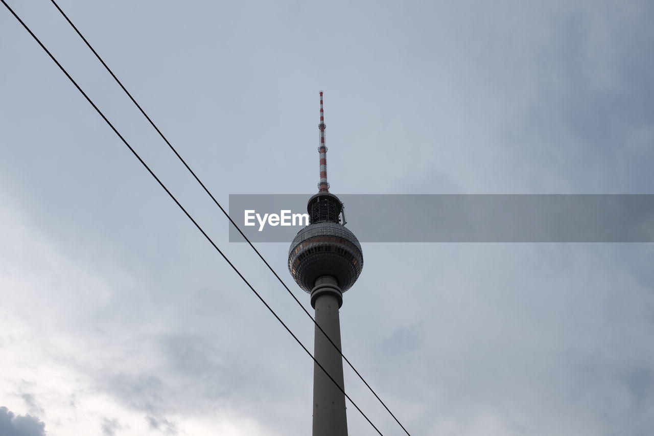 Low angle view of fernsehturm and power cables against sky