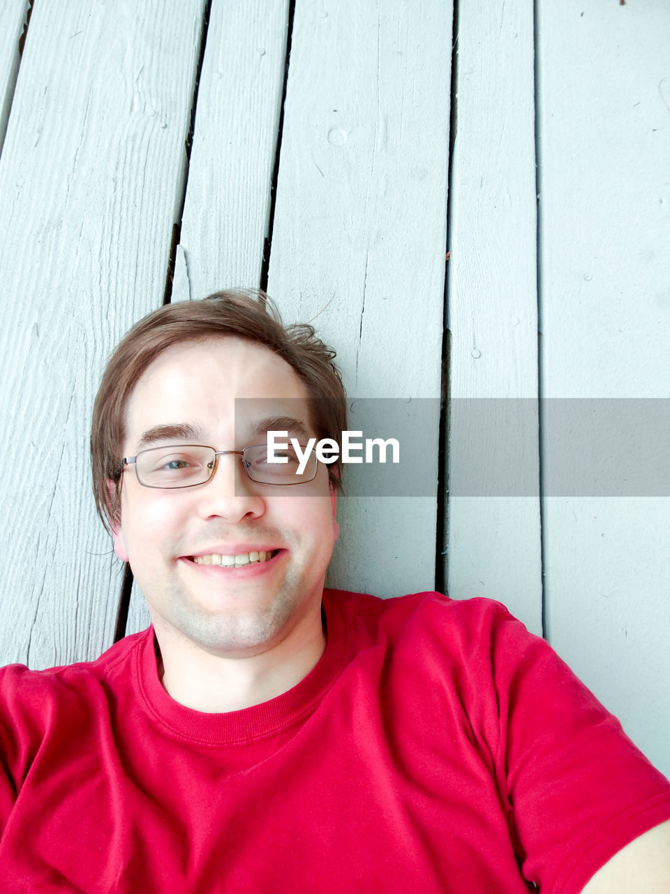 PORTRAIT OF SMILING YOUNG MAN WITH RED EYEGLASSES AGAINST WALL