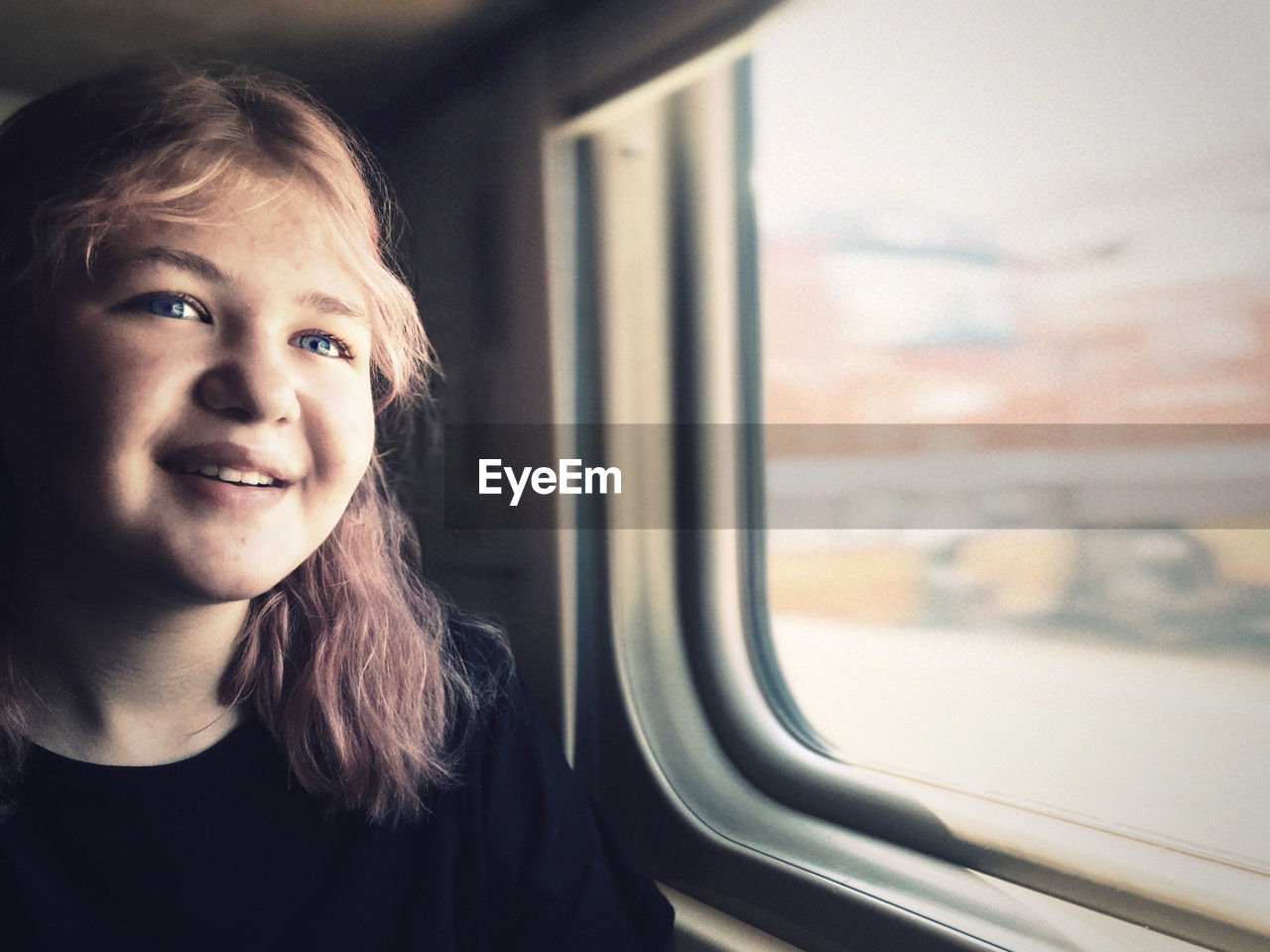 Smiling teenage girl sitting by window in train