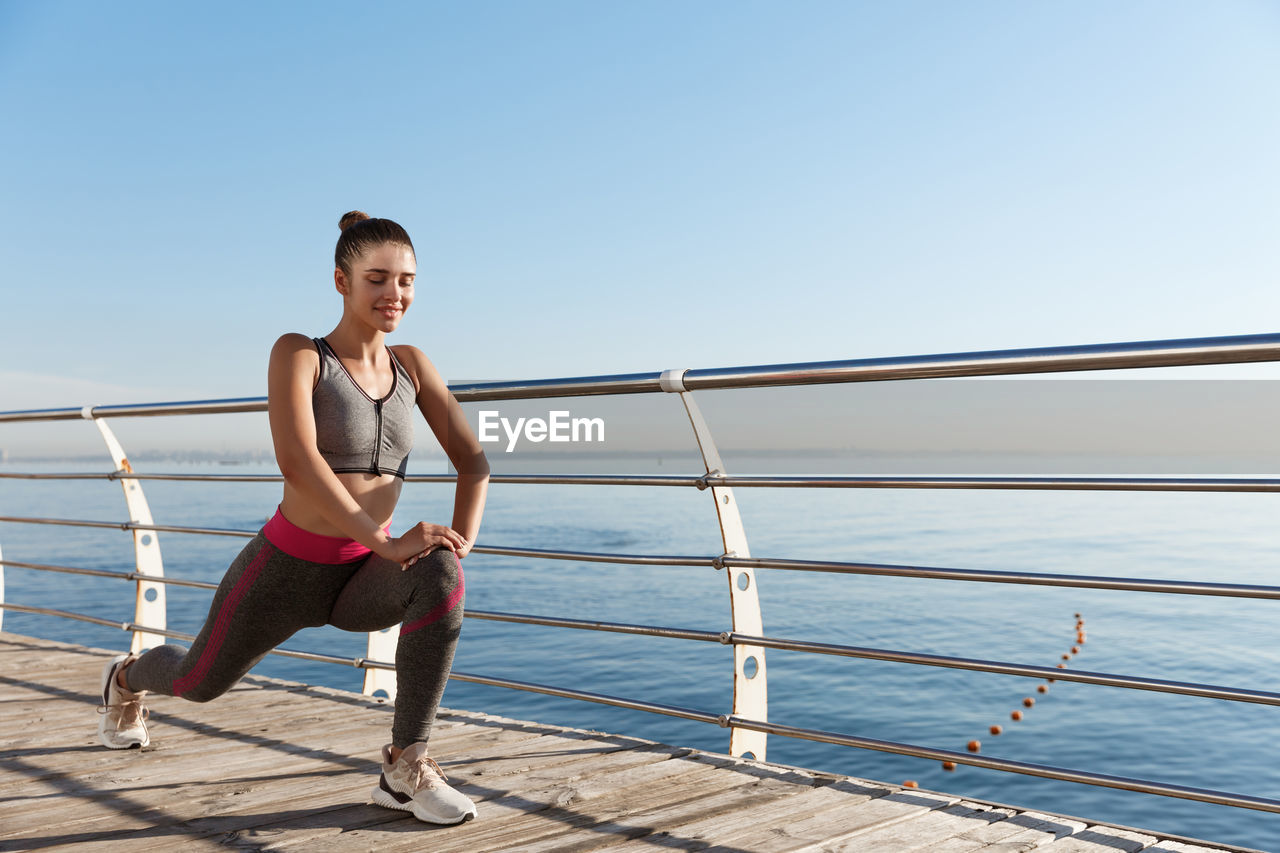 Woman standing by railing against sea against clear sky