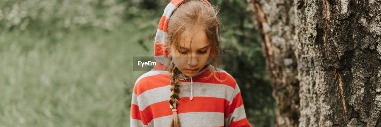 Portrait face of upset or focused thoughtful scowl eight year old kid girl in hood of striped hoodie