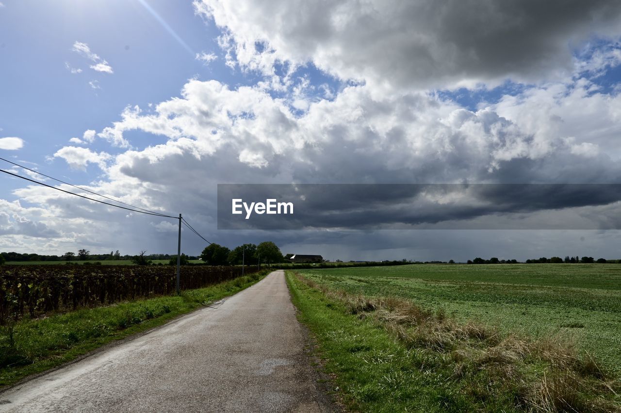 cloud, sky, landscape, environment, horizon, road, nature, plant, rural area, field, transportation, land, rural scene, grass, the way forward, beauty in nature, scenics - nature, no people, agriculture, cloudscape, diminishing perspective, vanishing point, sunlight, dirt road, outdoors, dirt, plain, dramatic sky, tranquility, storm, hill, day, morning, prairie, non-urban scene, tree, blue, travel, country road, street, crop, farm, tranquil scene