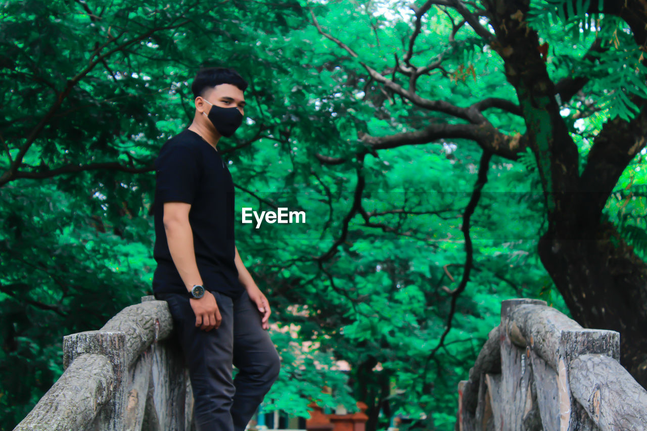 Young man wearing mask standing against tree