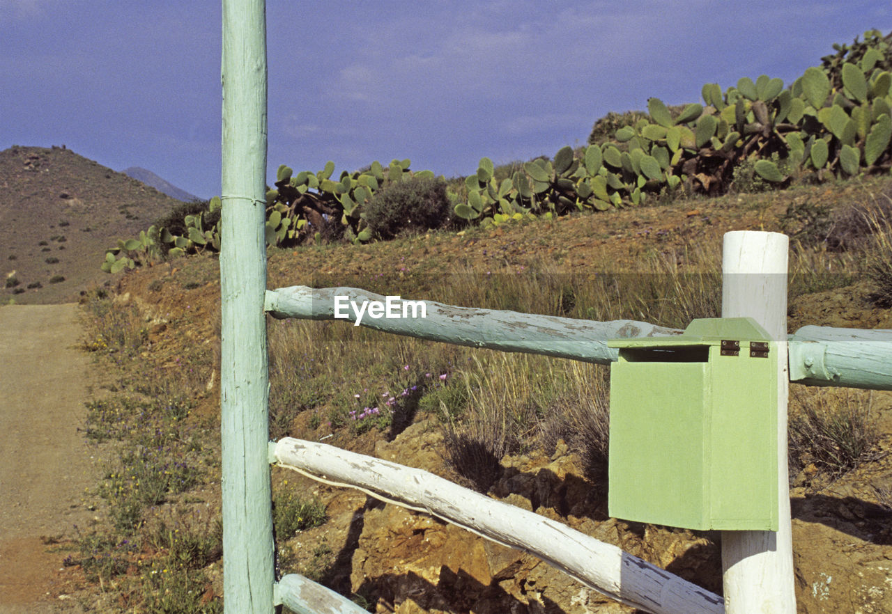 CLOSE-UP OF WOODEN POST ON LANDSCAPE AGAINST MOUNTAINS