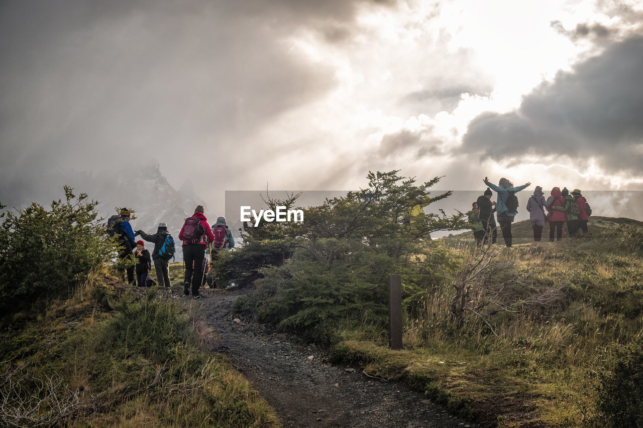 GROUP OF PEOPLE WALKING ON MOUNTAIN AGAINST SKY