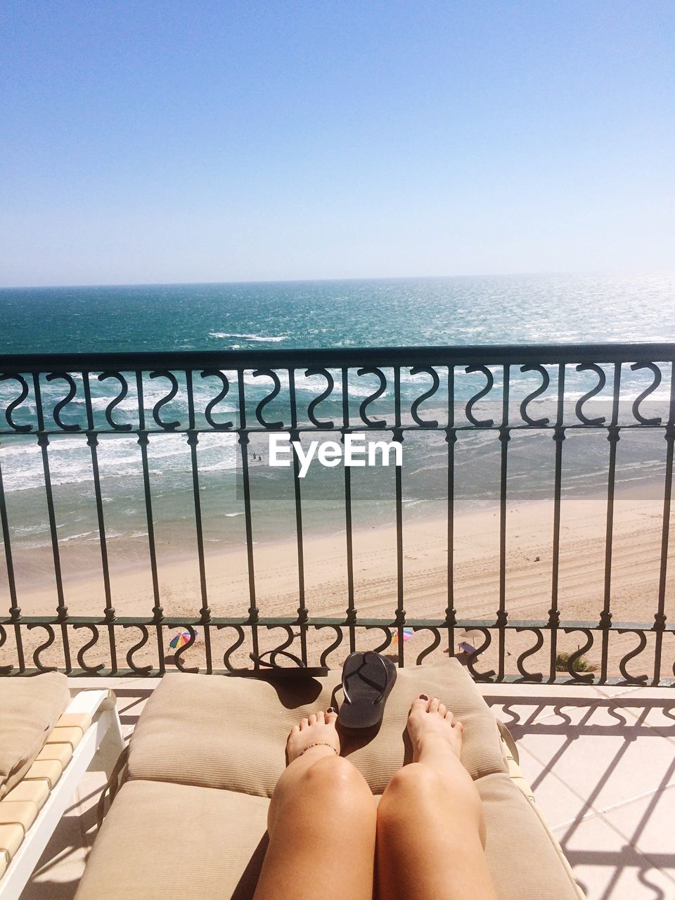 Low section of woman relaxing by railing at beach against clear sky