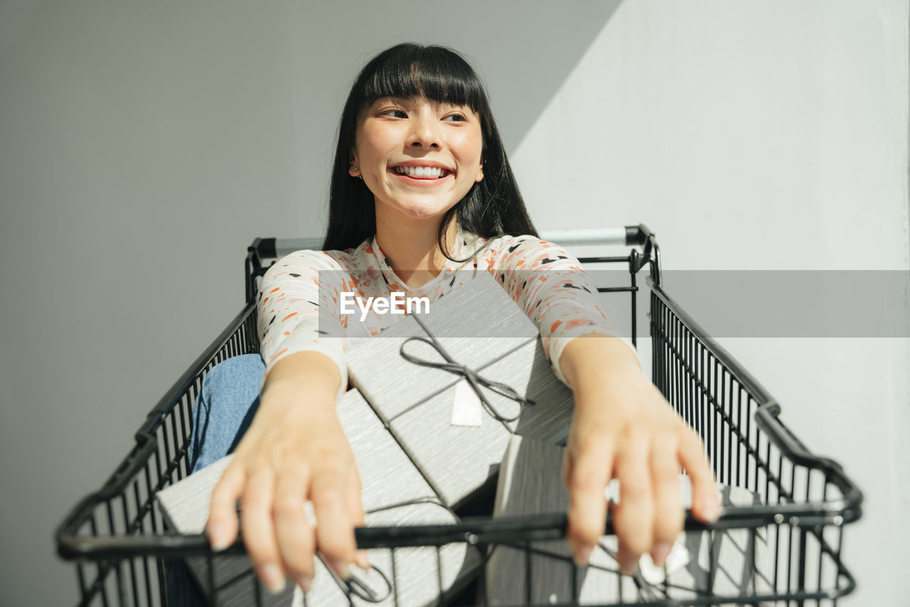 Smiling woman sitting in shopping cart outdoors