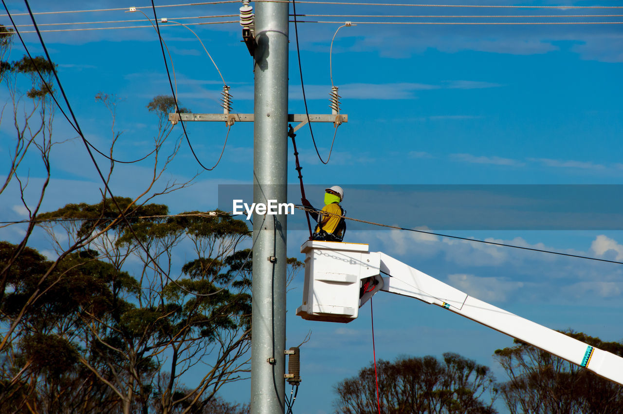Man working on electrical pole against sky