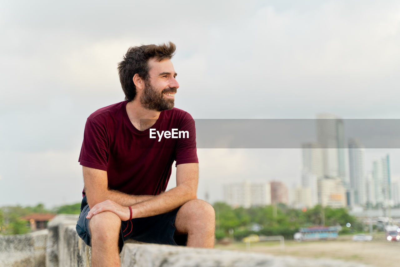 portrait of young man sitting on retaining wall