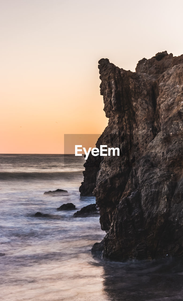 Rock formation on beach against sky during sunset