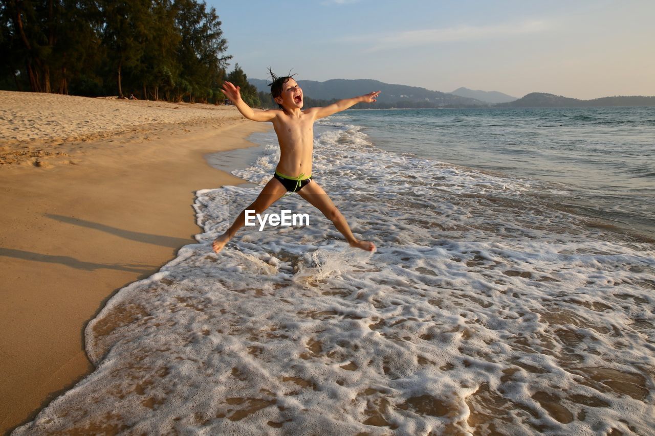 Full length of boy enjoying at beach against sky