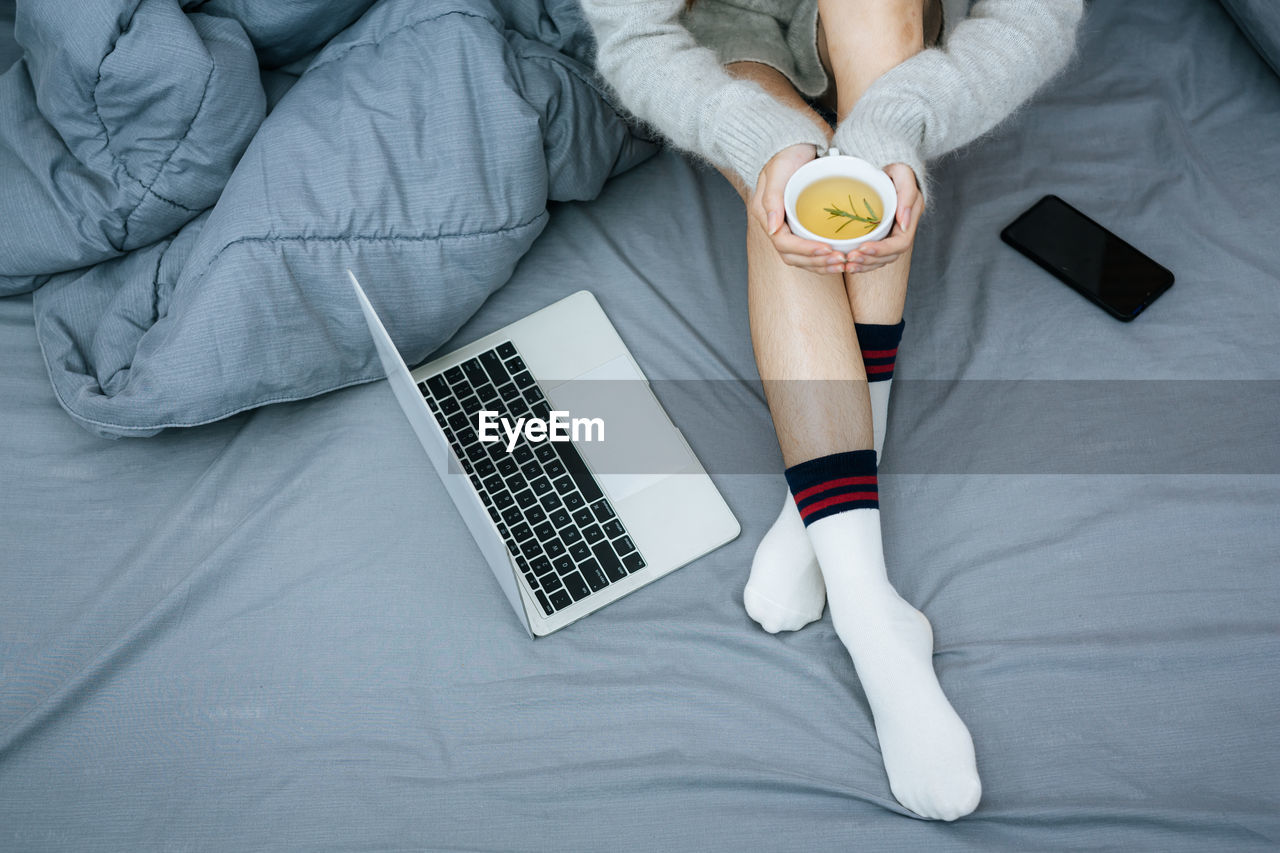 low section of woman using laptop on bed
