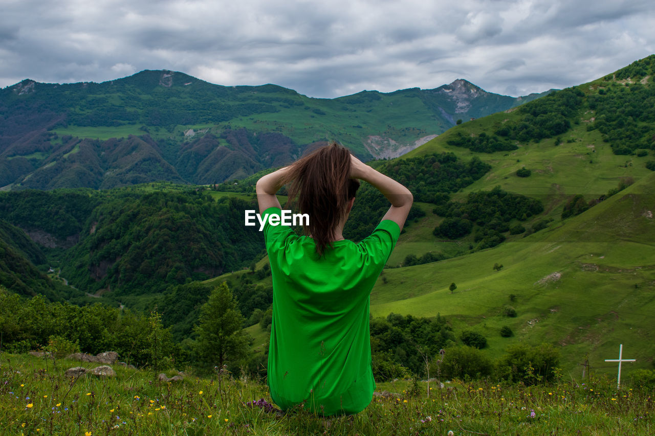 Rear view of woman with arms raised against mountain range