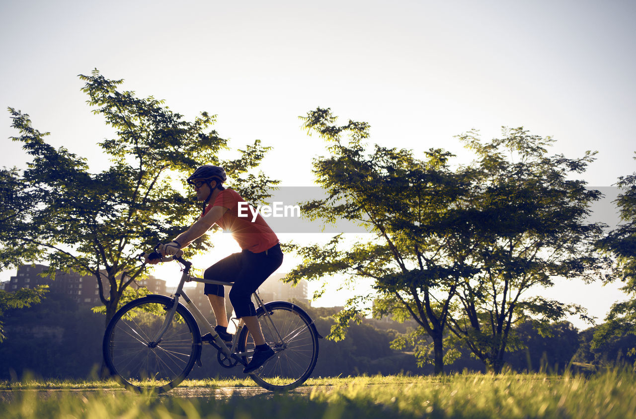 Side view of man cycling by trees against clear sky at park