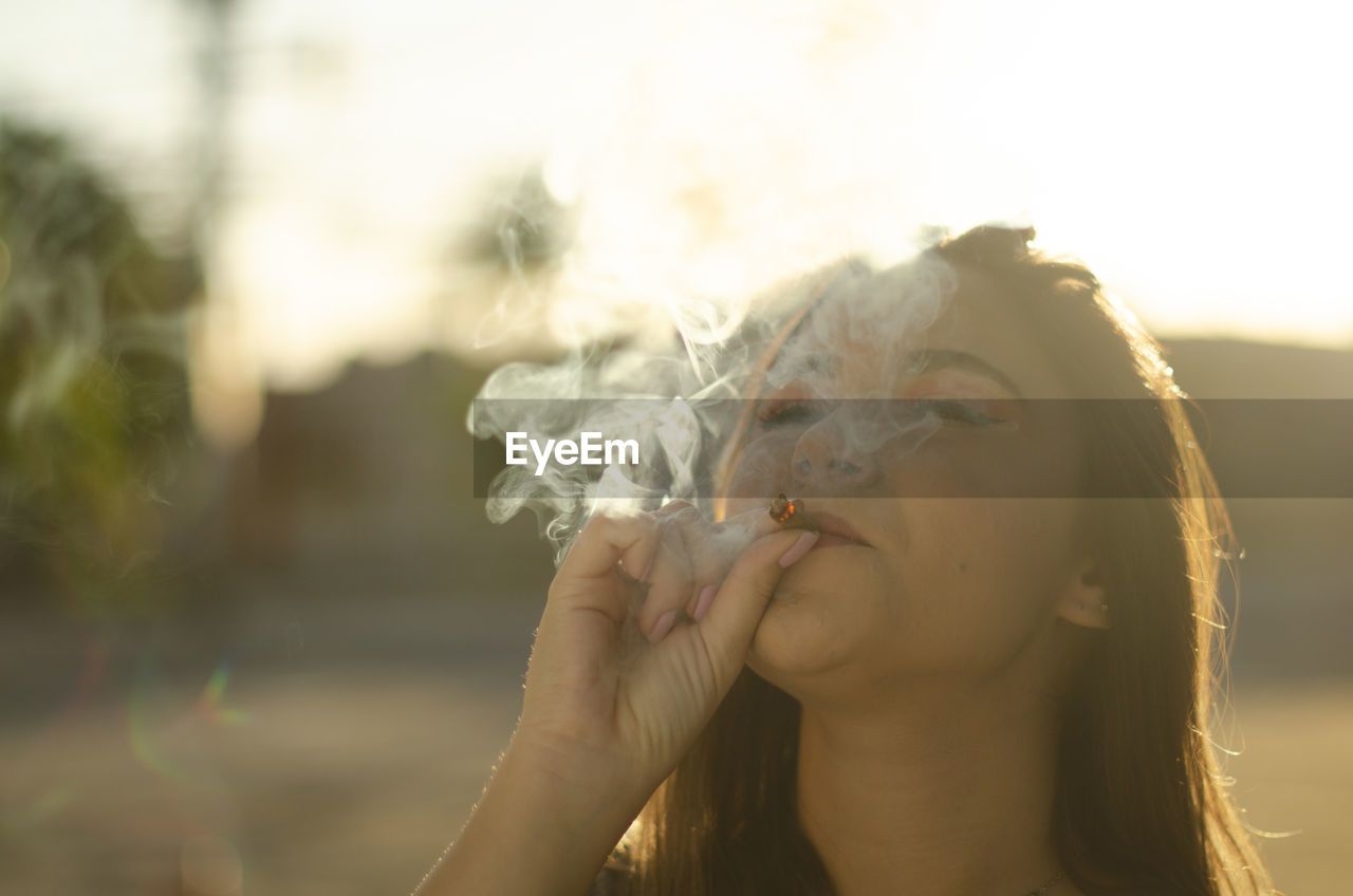 Close-up portrait of young woman smoking outdoors