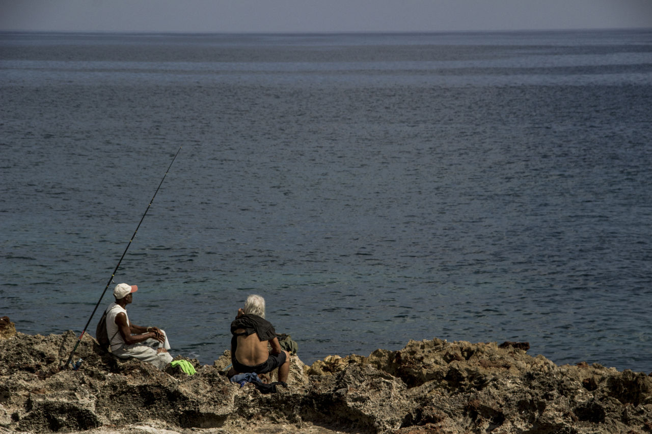 MAN FISHING ON ROCK BY SEA