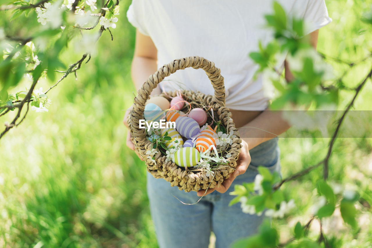 Funny teen girl with eggs basket and bunny ears on easter egg hunt in sunny spring garden