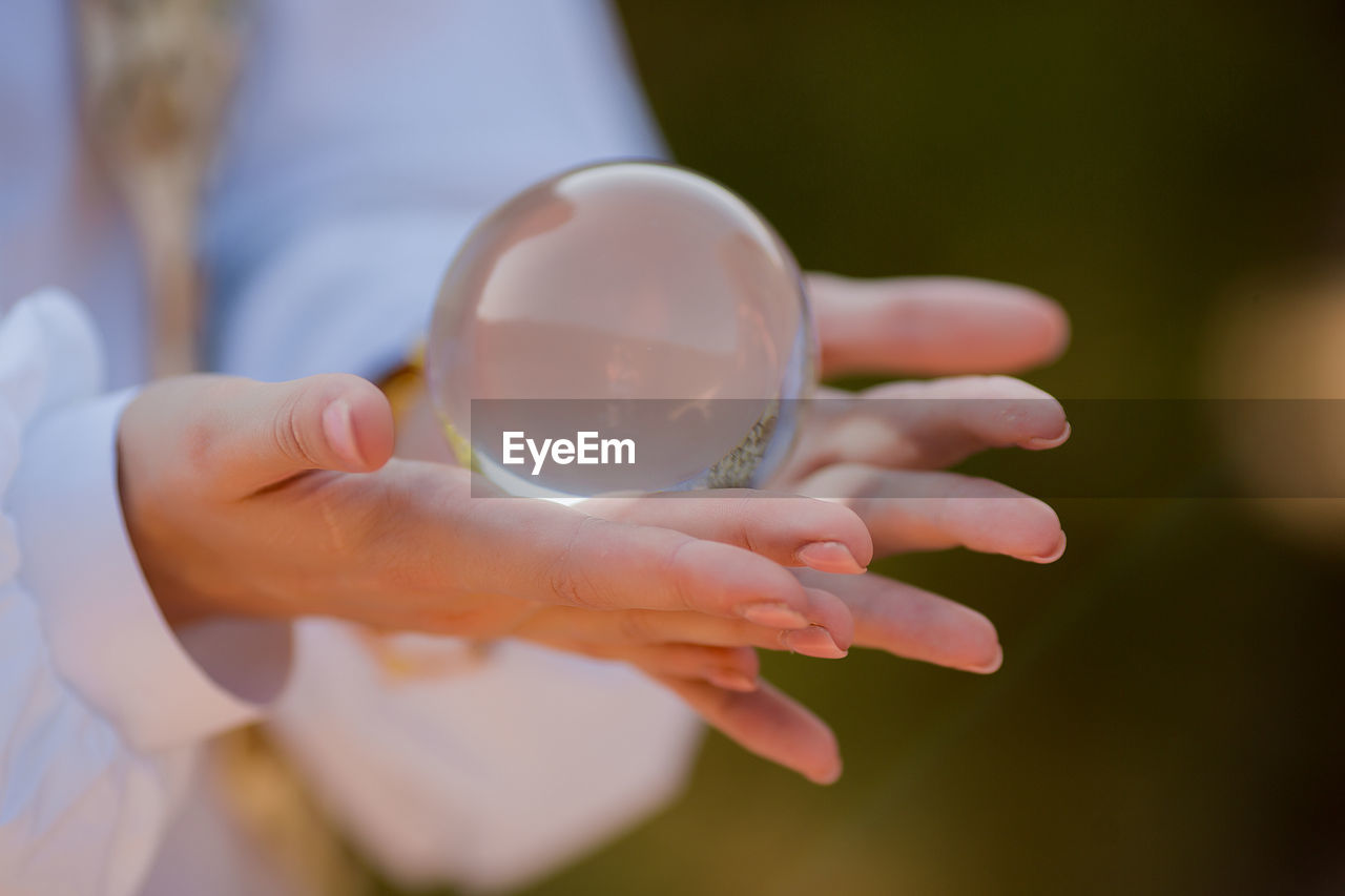 CLOSE-UP OF HAND HOLDING CRYSTAL BALL WITH REFLECTION OF MAN