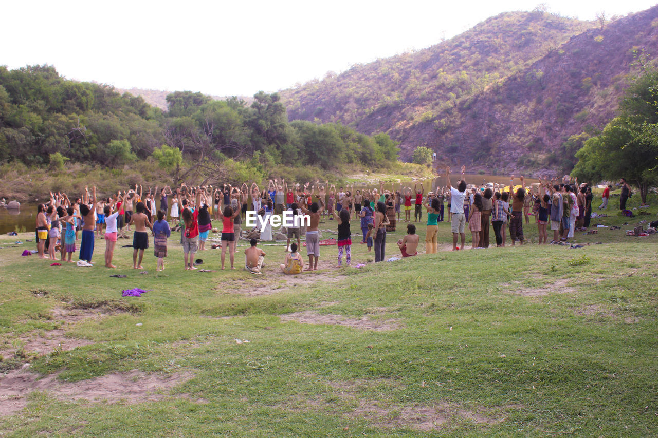 People standing with arms raised on grassy field during religious ceremony