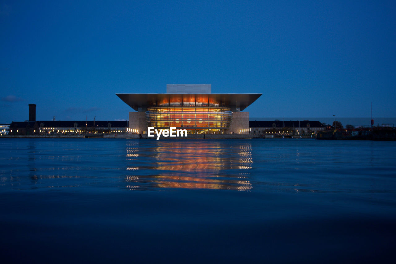 Illuminated building by sea against blue sky