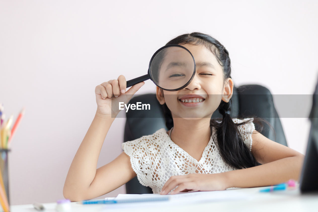 Portrait of cute girl looking through magnifying glass against white background