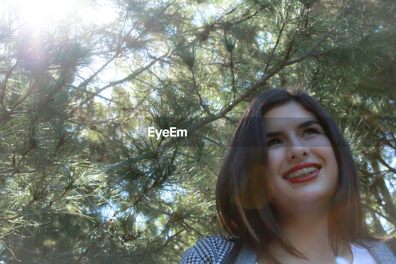 PORTRAIT OF SMILING WOMAN AGAINST TREES