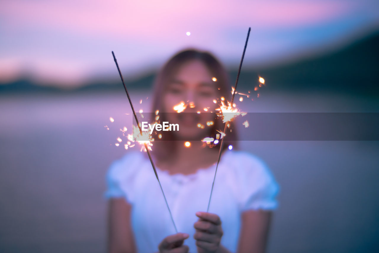 Portrait of woman holding sparkler against sky