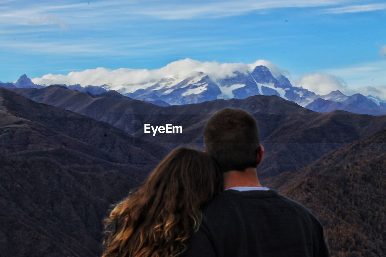 Rear view of couple looking at mountains against sky