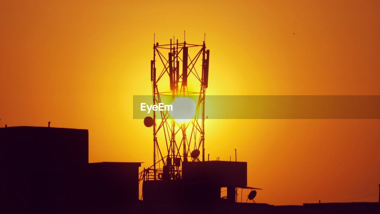 Low angle view of silhouette communications tower against orange sky