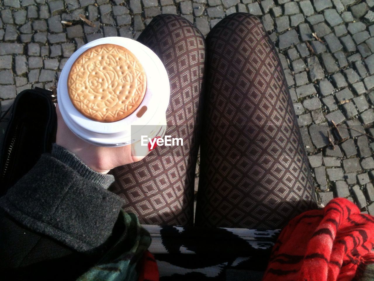 Low section of women holding disposable coffee cup along with biscuit