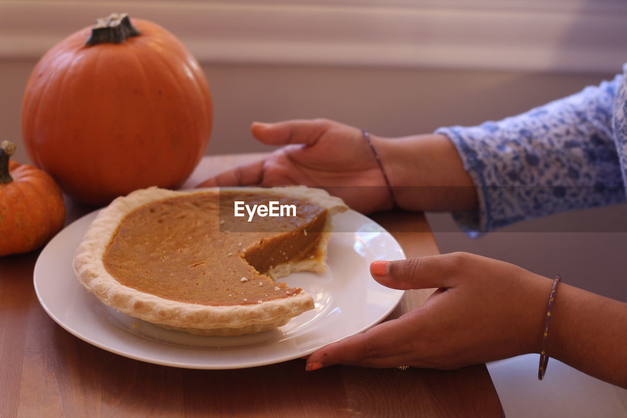 Cropped image of woman having pumpkin pie on table